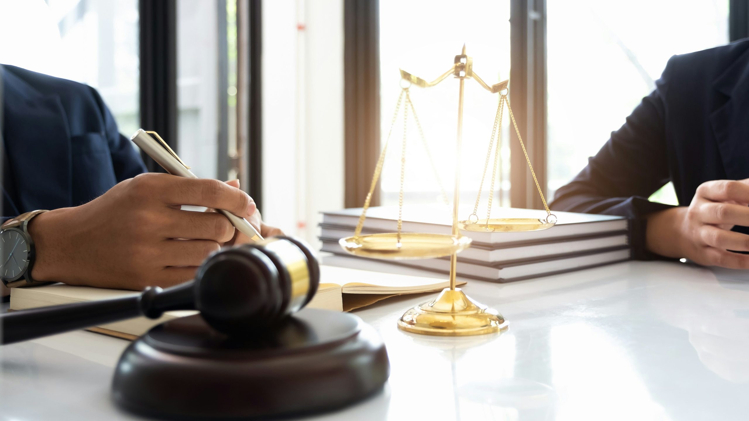 gavel, gold scales and two people meeting at a desk.